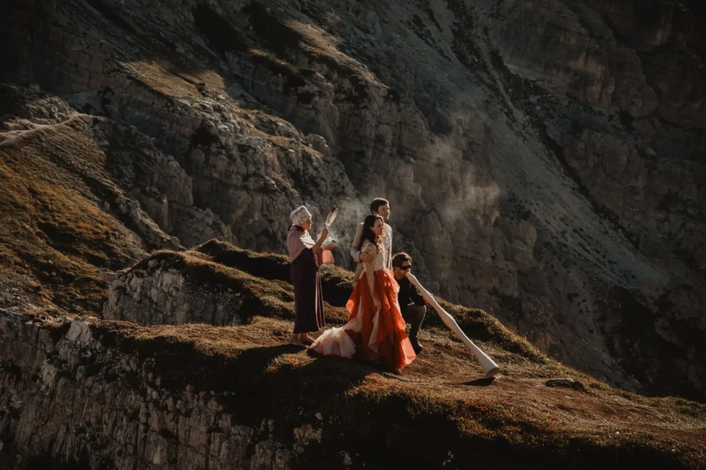 Couple on a rocky mountain ledge with musicians playing a frame drum and a didgeridoo.