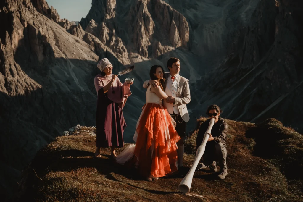 Couple exchanging vows with a celebrant and musician on a mountain ridge.