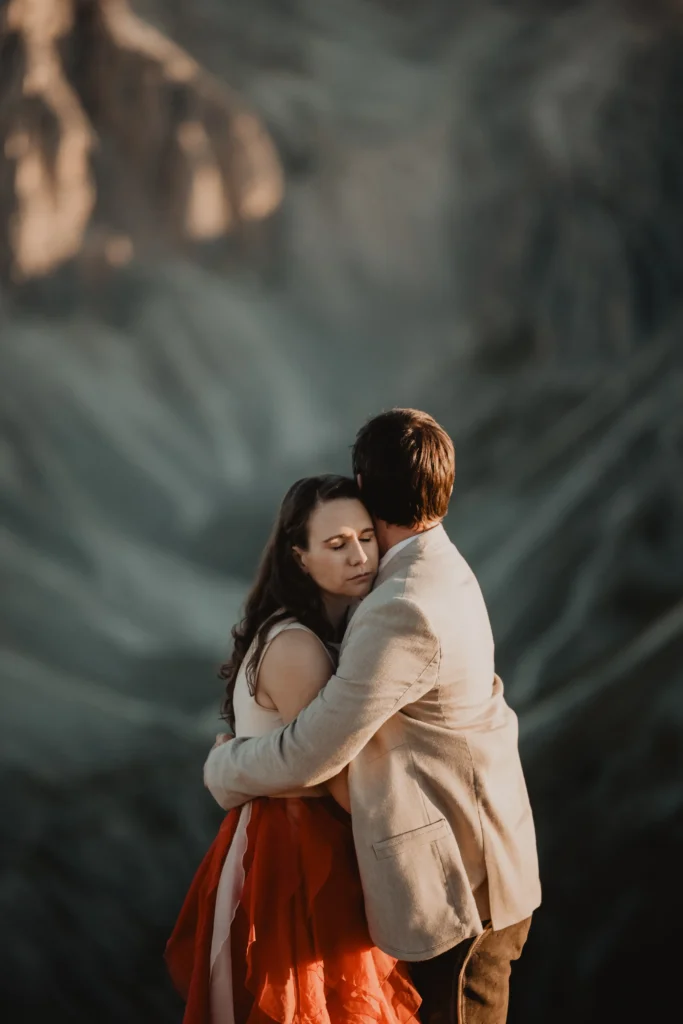 Couple embracing in warm evening light beneath steep mountain cliffs.