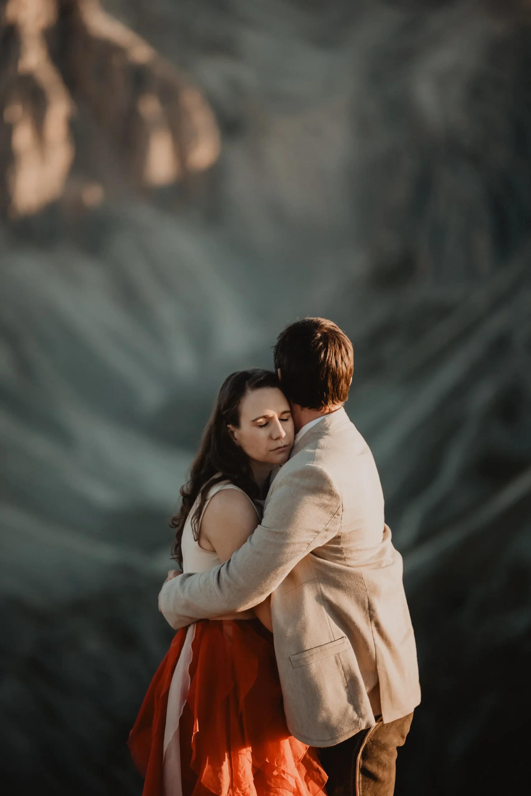Couple embracing in warm evening light beneath steep mountain cliffs.