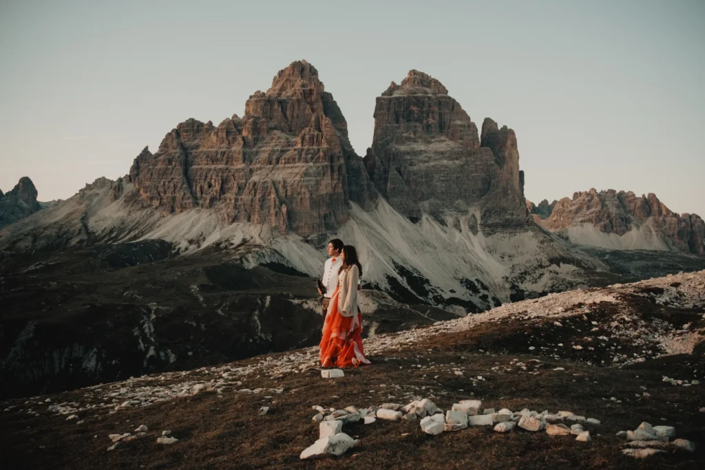 Couple standing together on a rocky plateau beneath the towering peaks of the Dolomites.