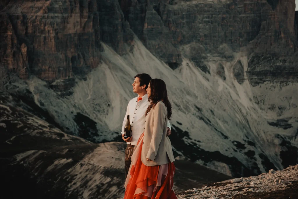 Couple looking across a mountain valley, the bride wearing an orange skirt.