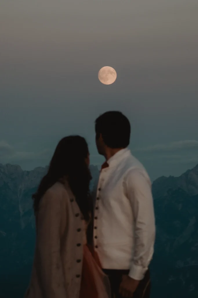 Couple looking towards the moon above the mountains.