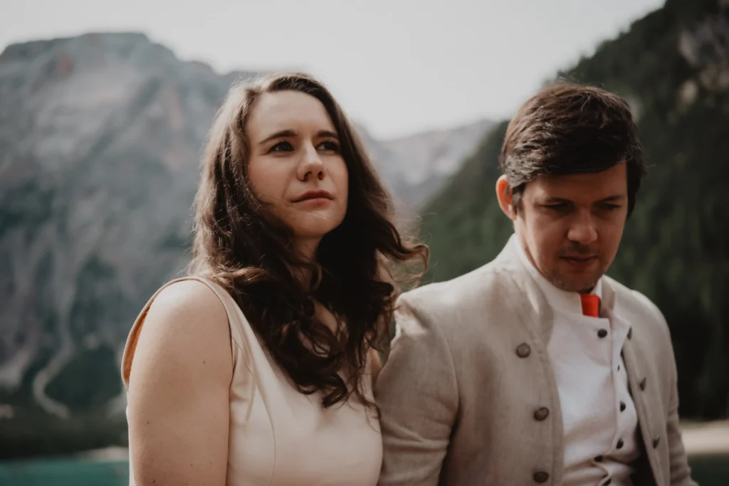 Portrait of a couple beside a lake surrounded by mountains.