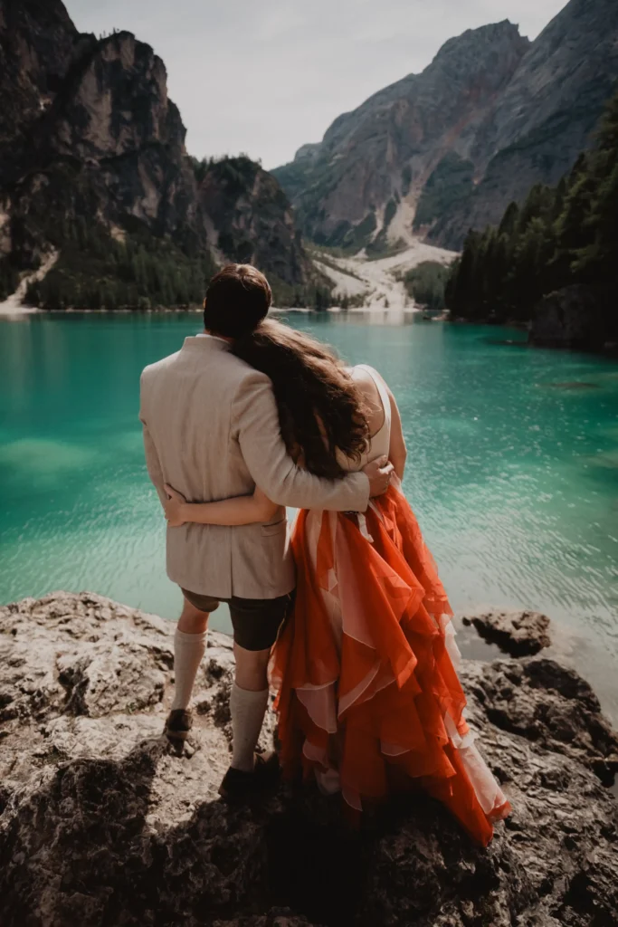 Couple viewed from behind beside the lake, the bride in an orange skirt.