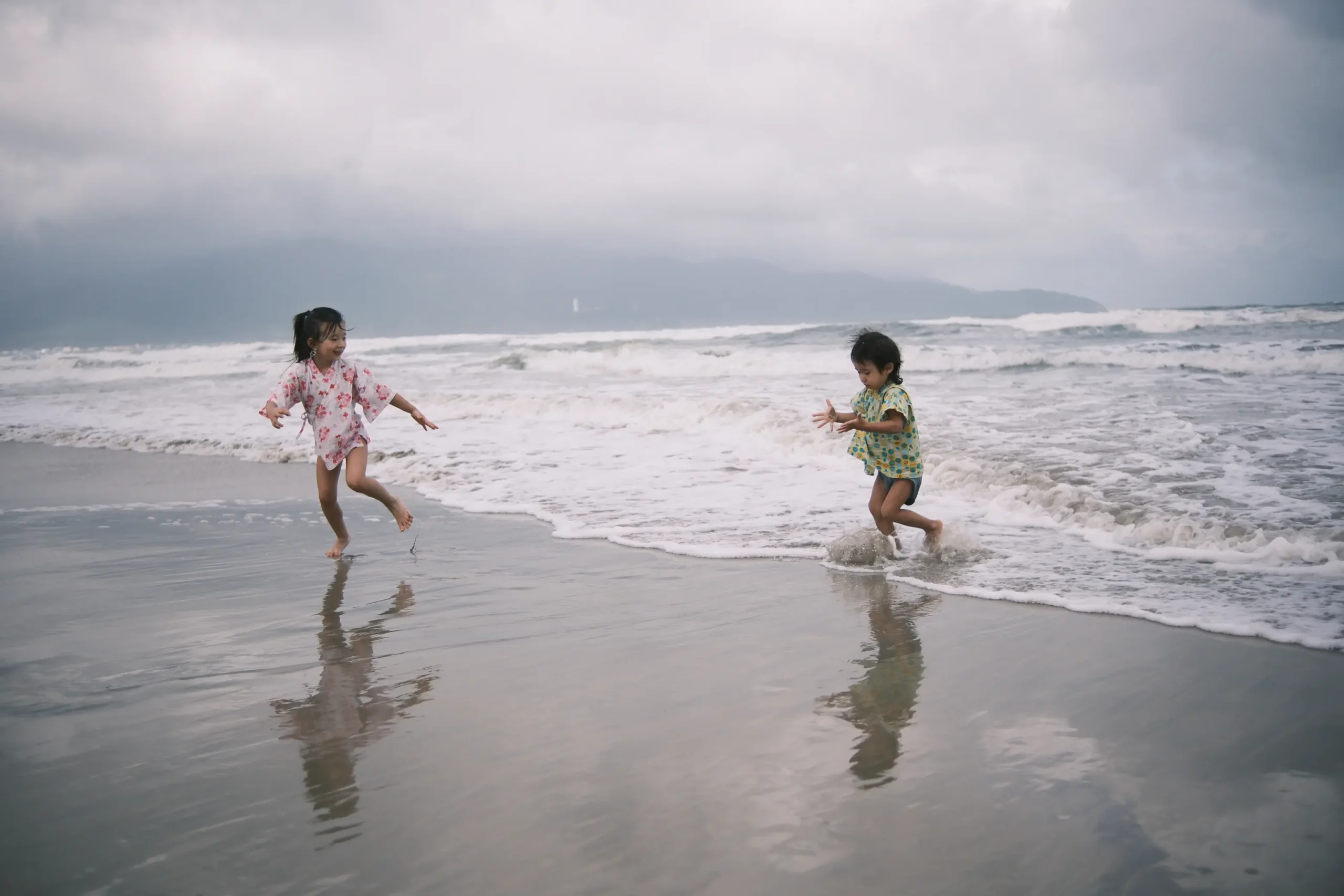 Zwei Kinder spielen in den Wellen an einem Sandstrand.
