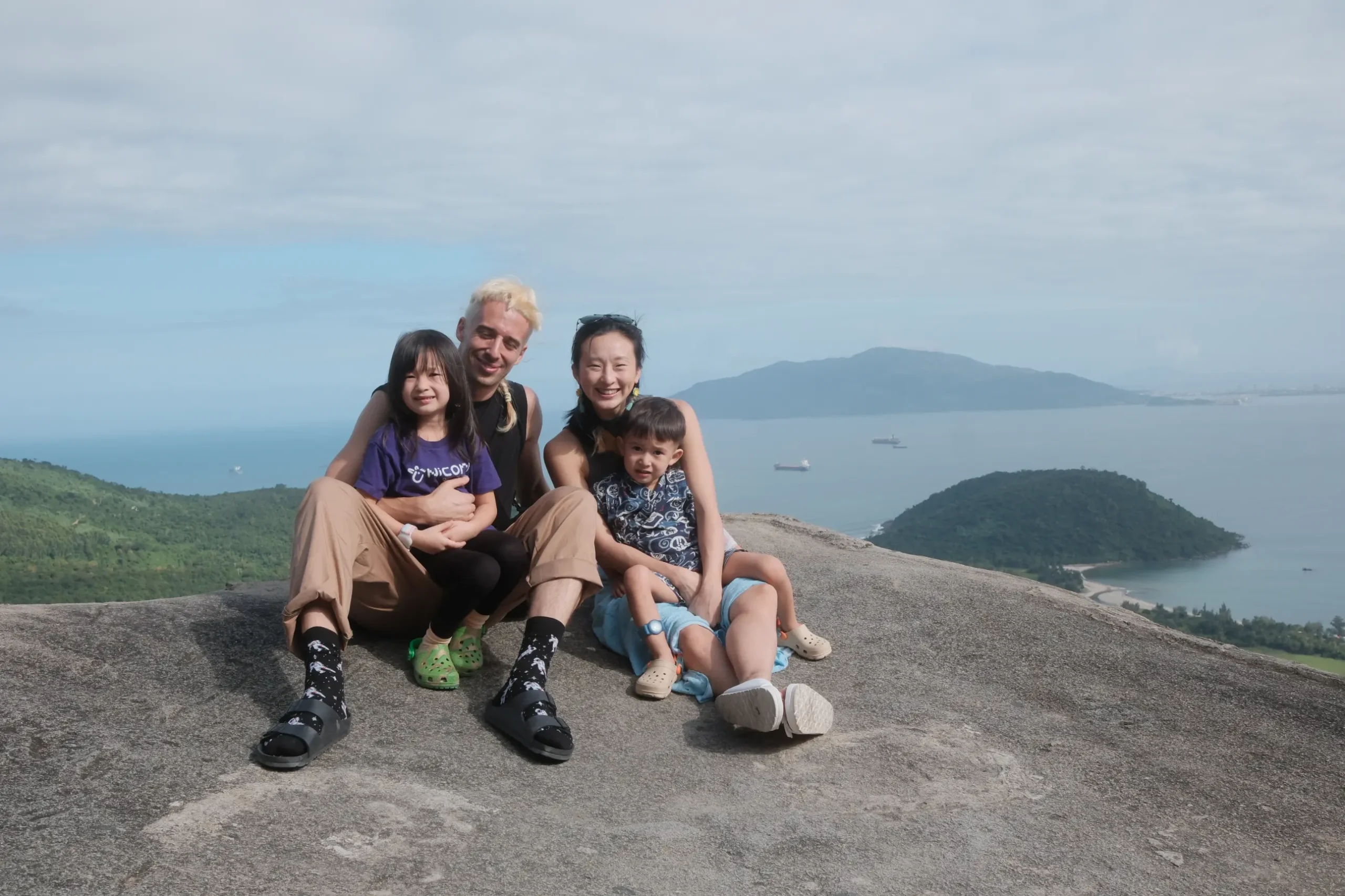 Vierköpfige Familie sitzt an einem felsigen Aussichtspunkt über dem Meer.
