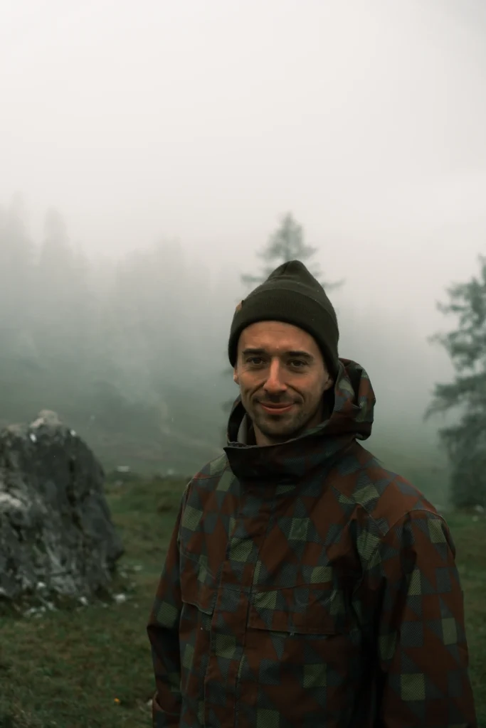 Portrait of Elias wearing a hat in a misty forest.