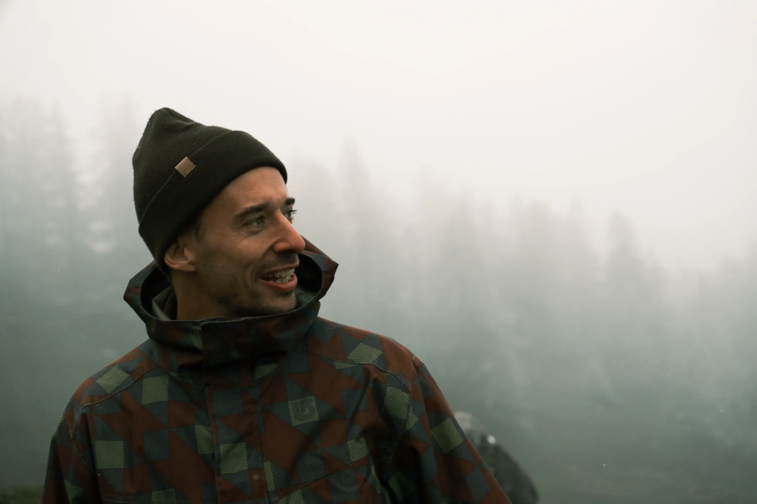 Elias mit Mütze und Wanderjacke im Freien vor nebligen Bäumen.
