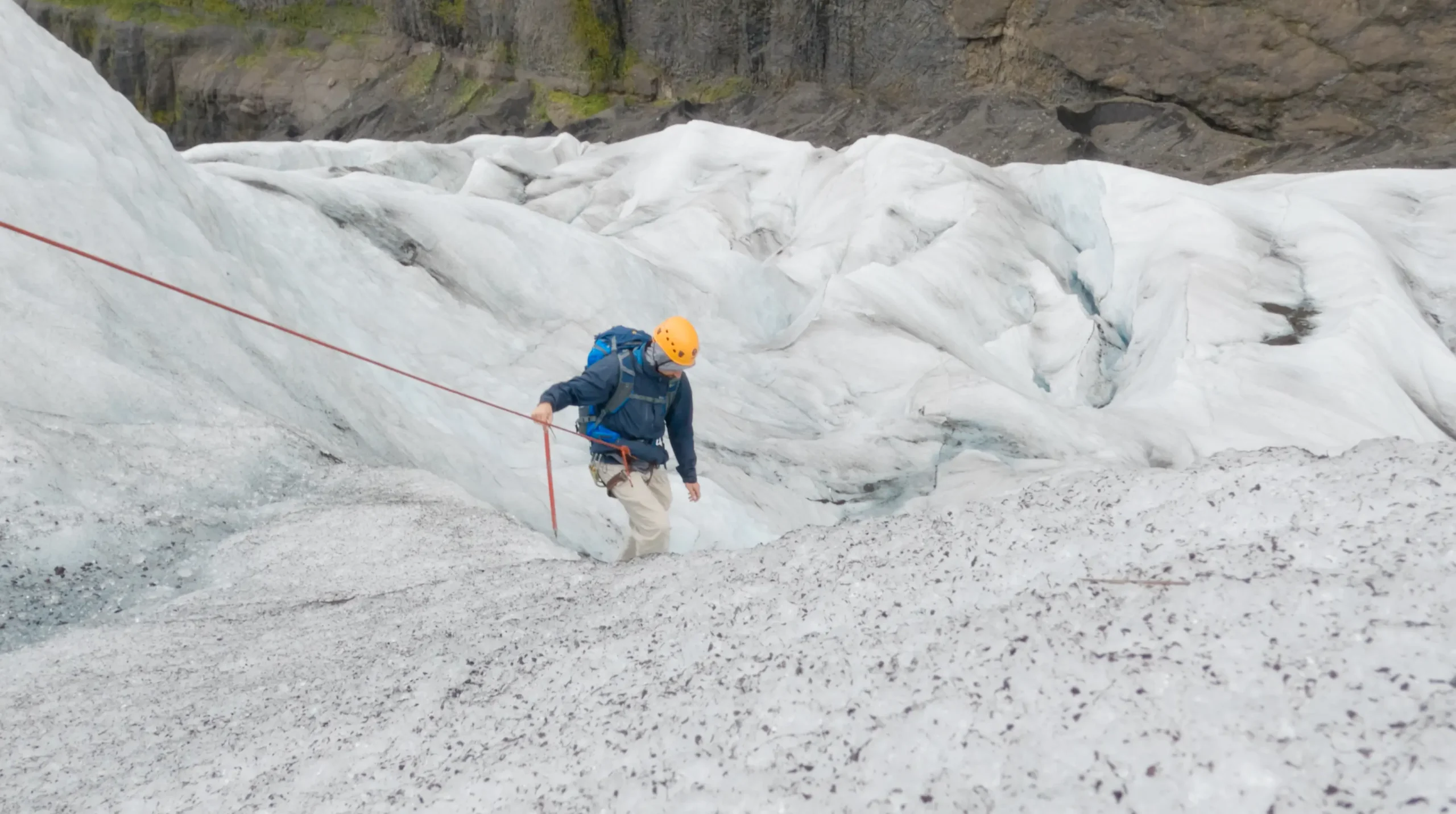 Bergsteiger mit Helm und Klettergurt überquert am Seil Gletschereis.