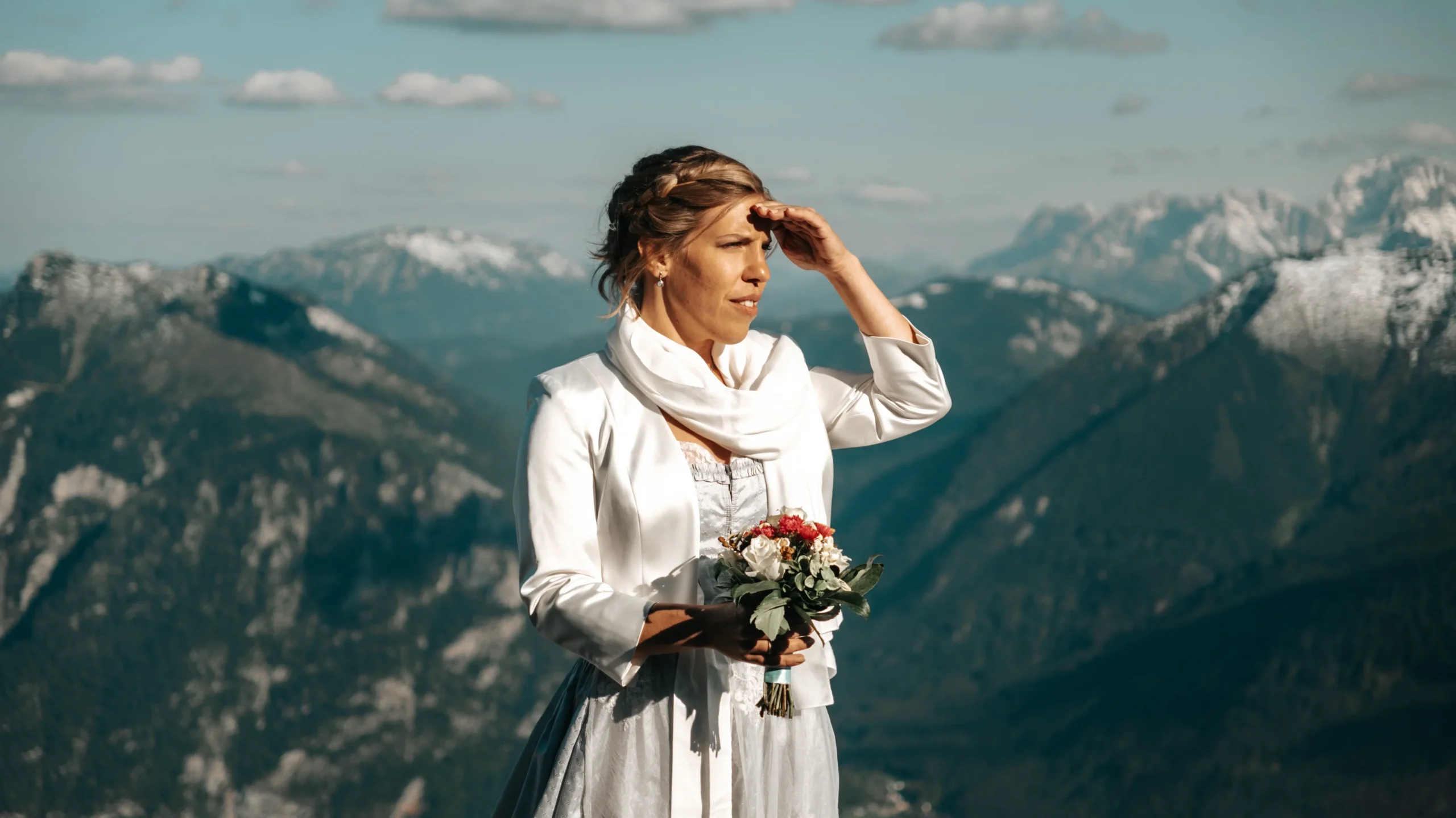 Braut mit einem Blumenstrauß vor einer weiten Berglandschaft.
