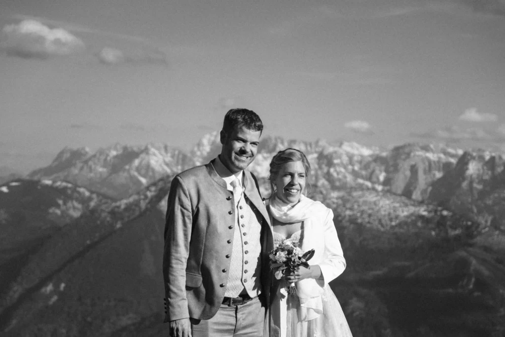 Black-and-white portrait of a couple in traditional clothing against a mountain panorama.