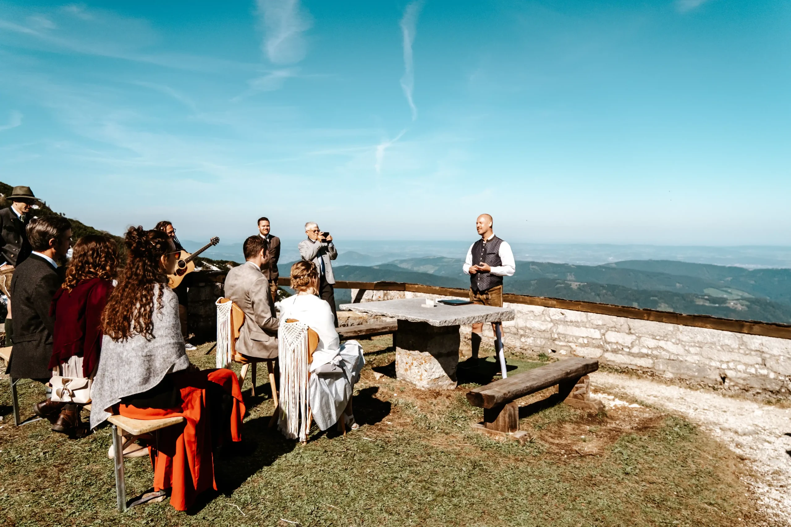Hochzeitsgäste sitzen bei einer Zeremonie auf einer Bergterrasse.