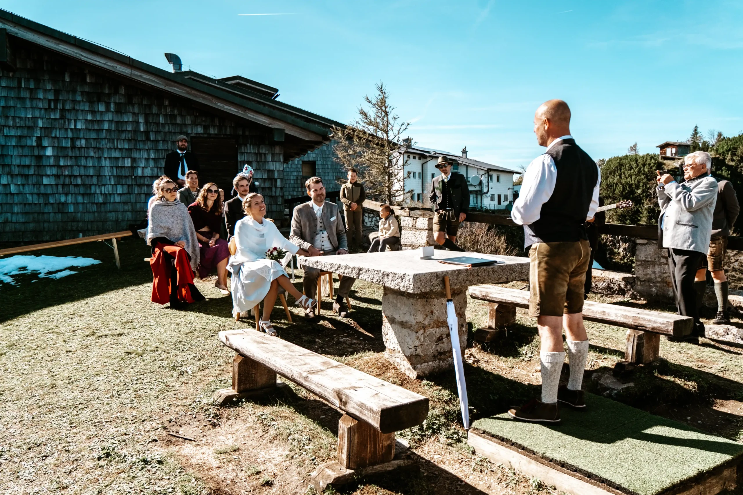 Trauredner spricht zu einem Paar neben einem Steintisch auf einer Bergterrasse.