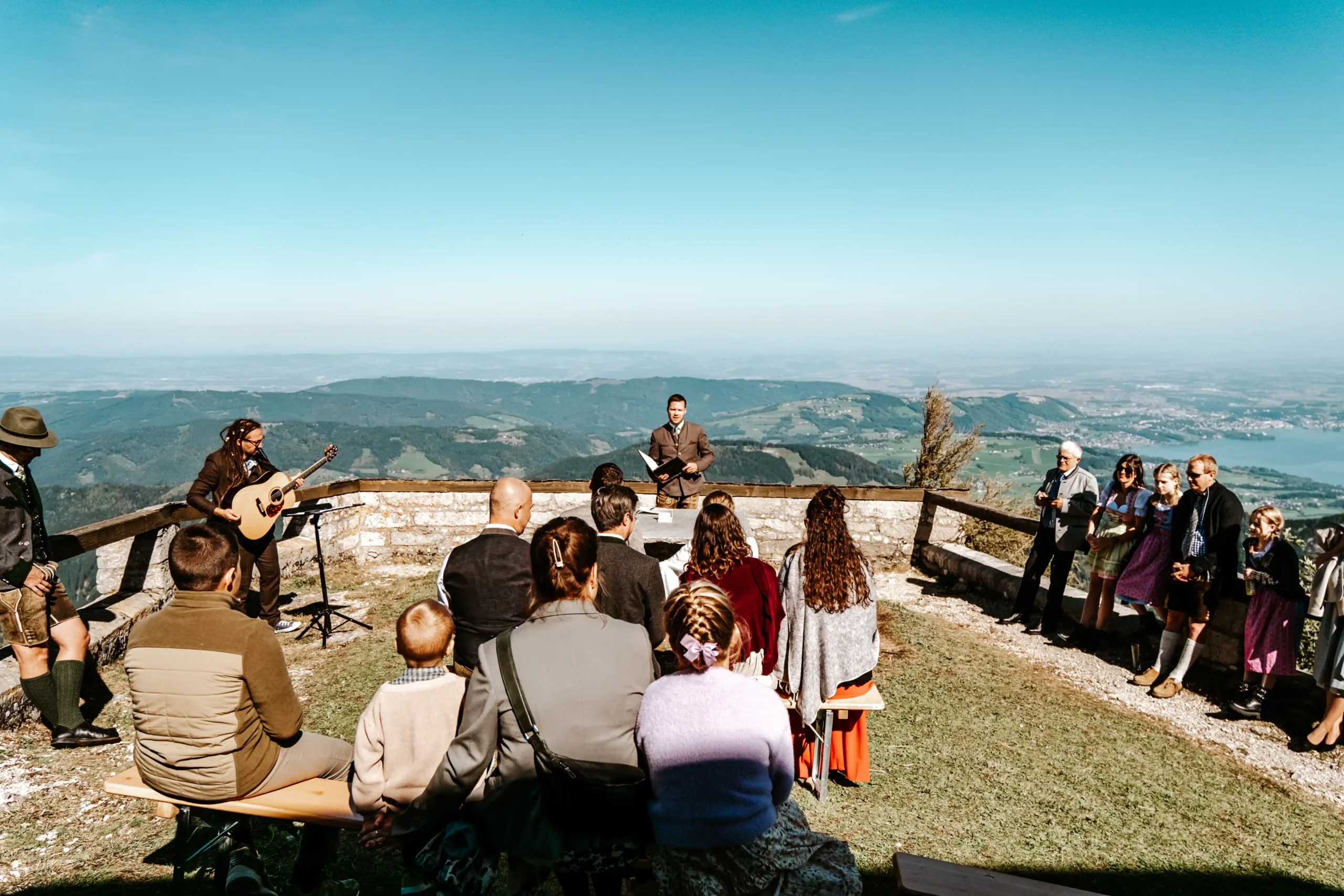 Hochzeitszeremonie mit Gästen auf einer Bergterrasse im Freien.