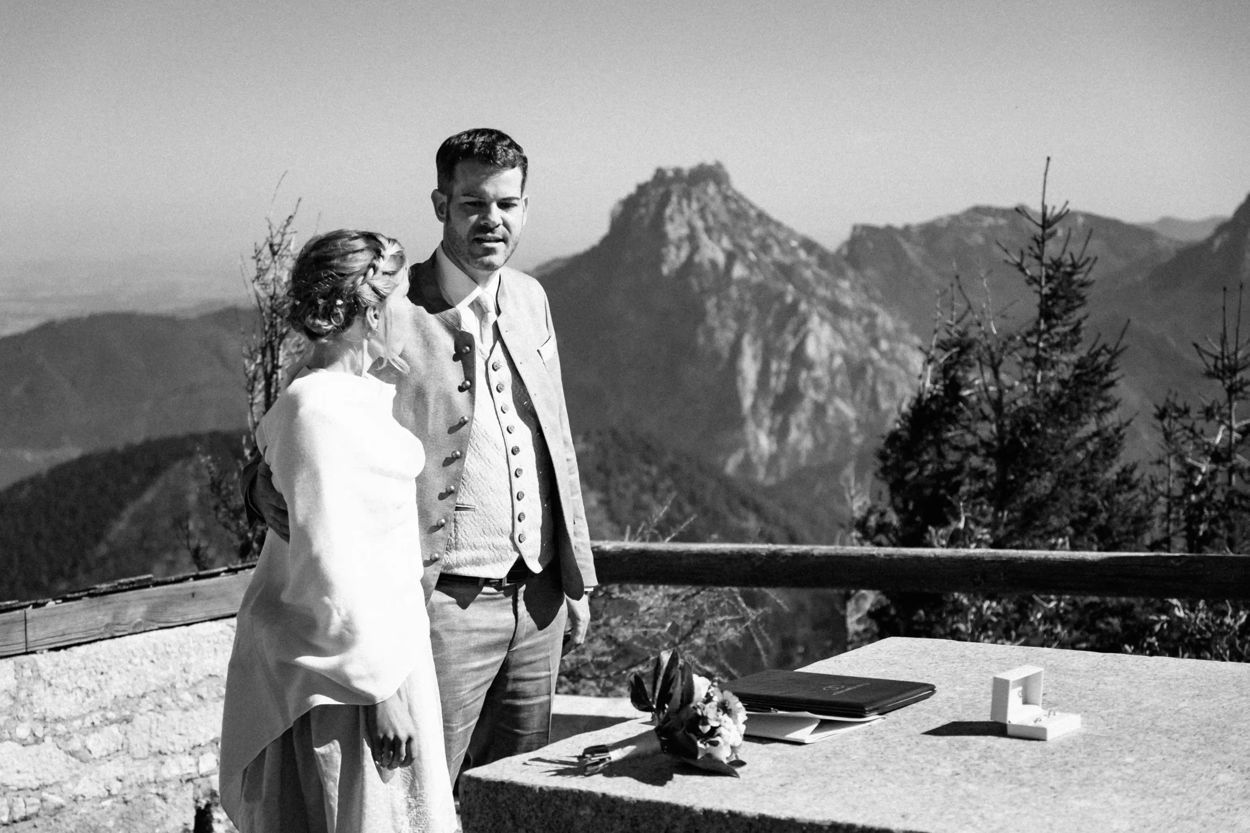 Schwarz-Weiß-Foto eines Paares neben einem Steintisch mit Blick auf die Berge.