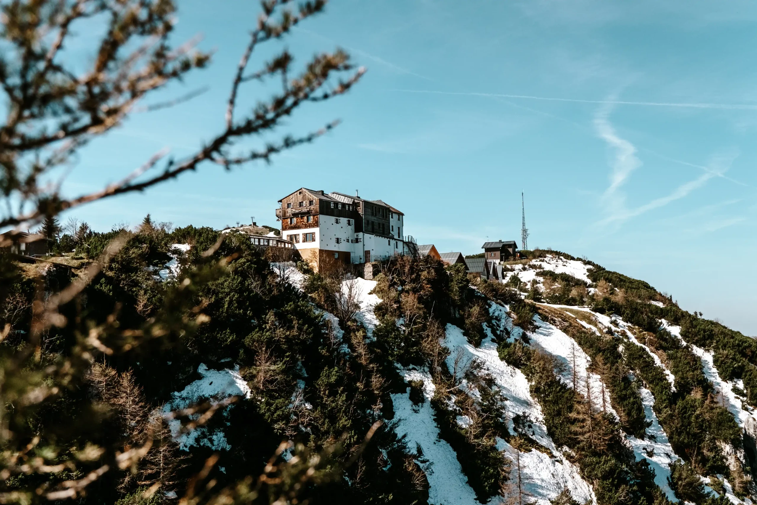 Berghütte auf einem felsigen Gipfel mit Schneeflecken.