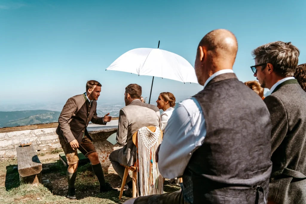 Guests watching a couple beneath a white umbrella during an outdoor ceremony.
