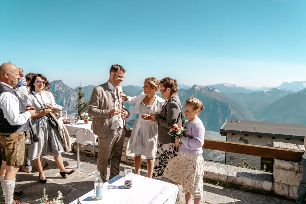 Couple celebrating with guests on a sunny terrace overlooking the mountains.