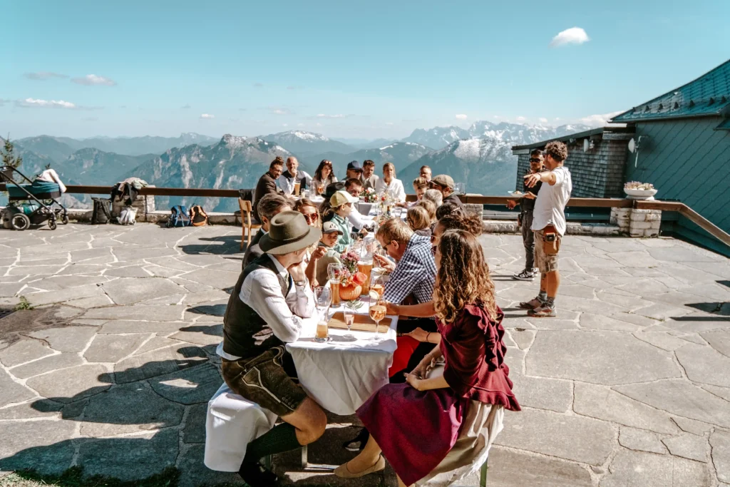 Wedding guests sharing a meal at a long table on a mountain hut terrace.