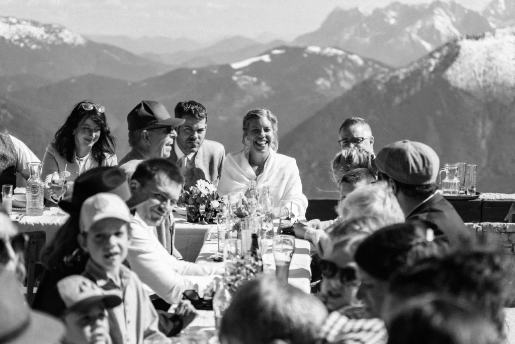 Wedding couple and guests gathered around a table on a mountain terrace.