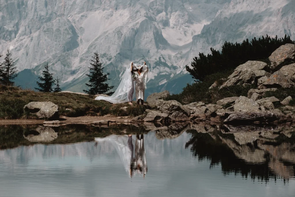 Couple reflected in a still mountain lake beneath rocky peaks.