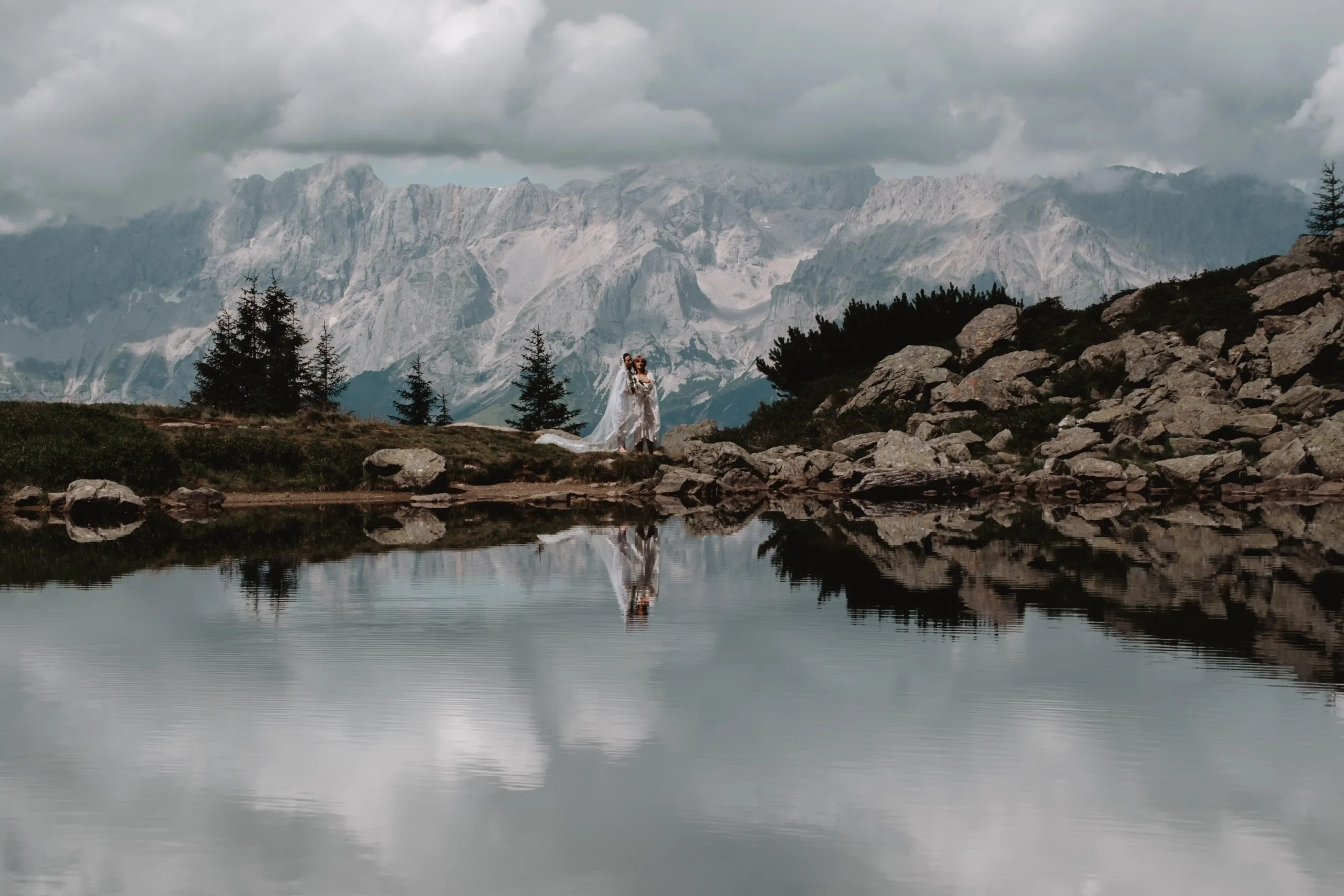 Braut an einem Bergteich, in dem sich die umliegenden Berge spiegeln.