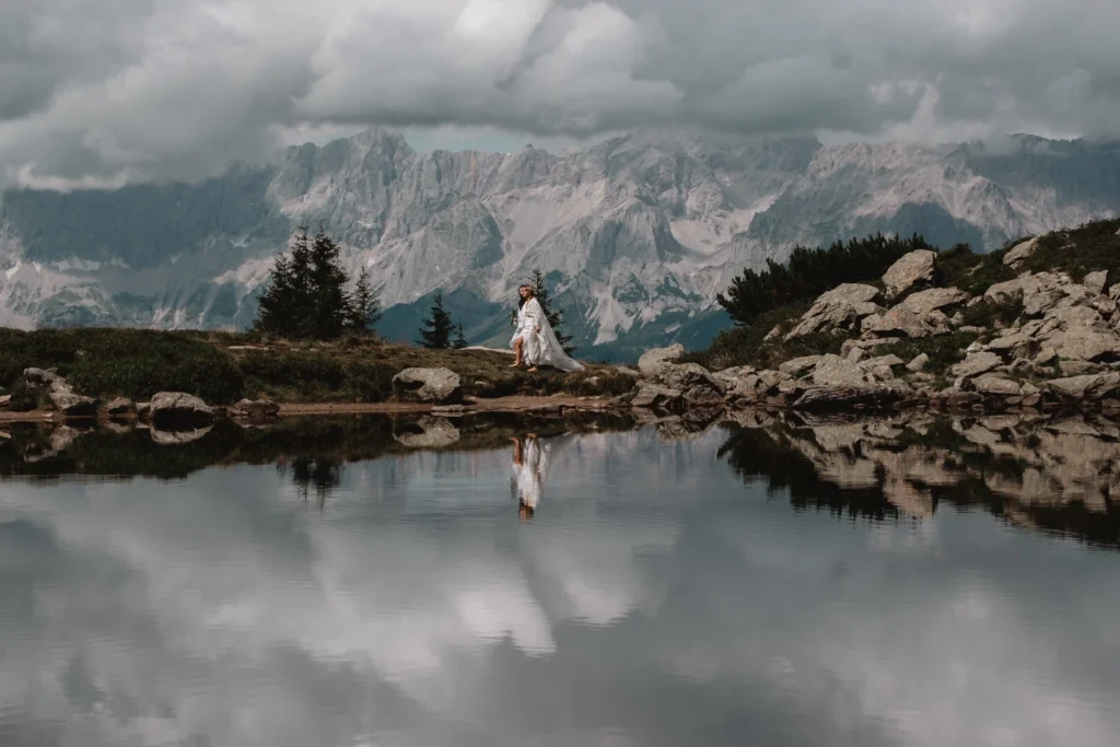Couple beside a mountain lake, with dark clouds reflected in the water.