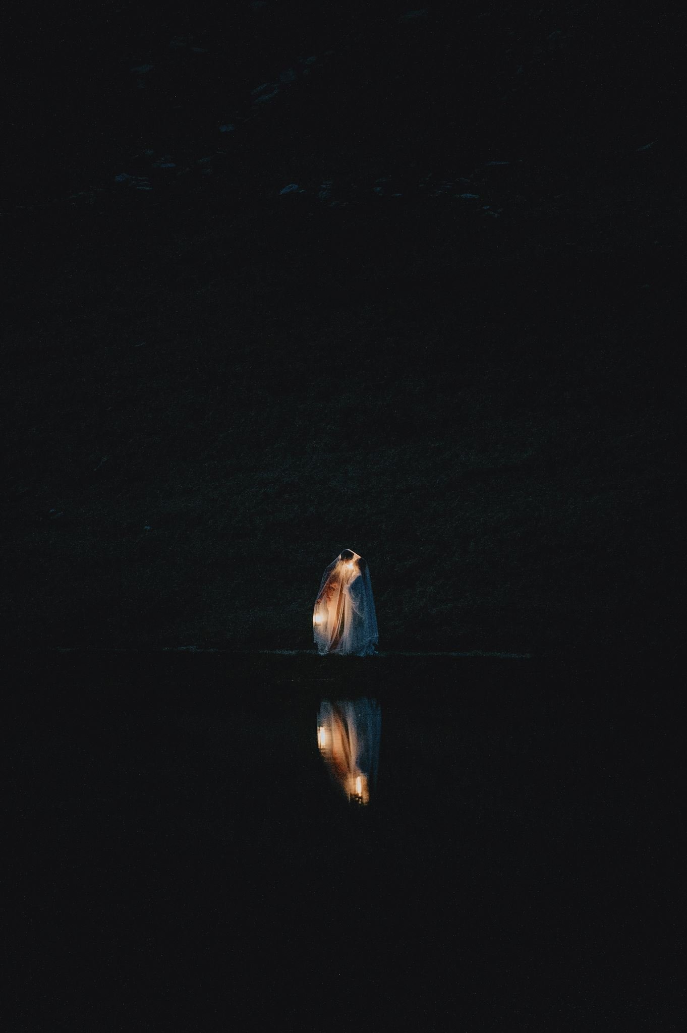 Beleuchtetes Paar in der Dunkelheit mit Spiegelbild im ruhigen Wasser.