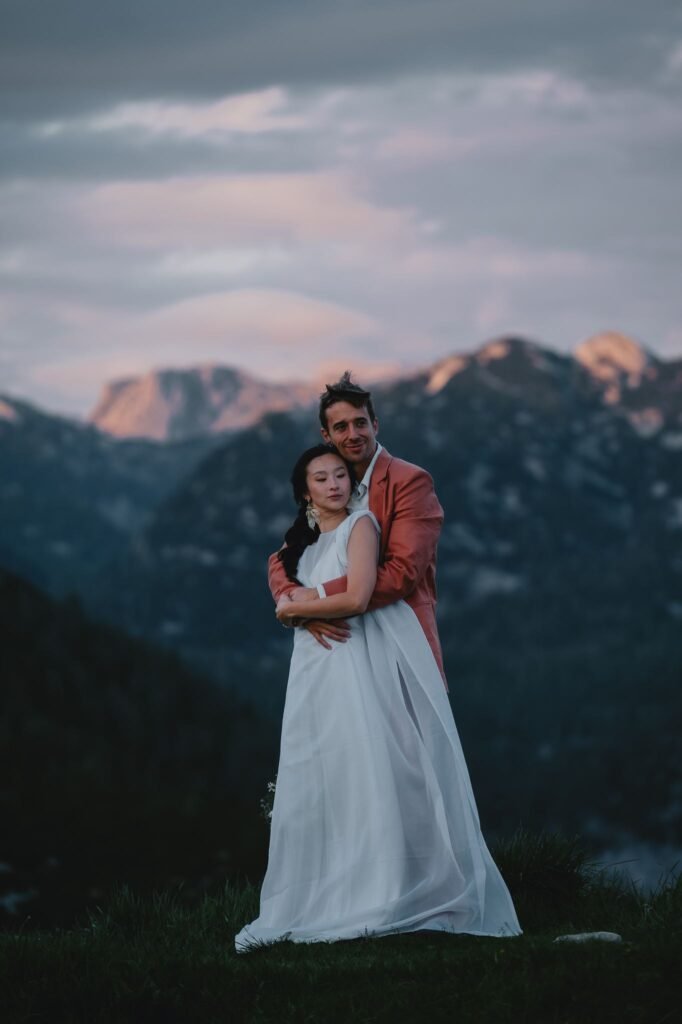 Portrait of Elias and Wendy with mountains and a pink evening sky behind them.