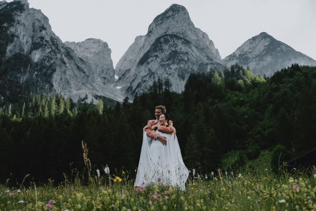 Elias and Wendy embracing in a meadow beneath jagged mountain peaks.