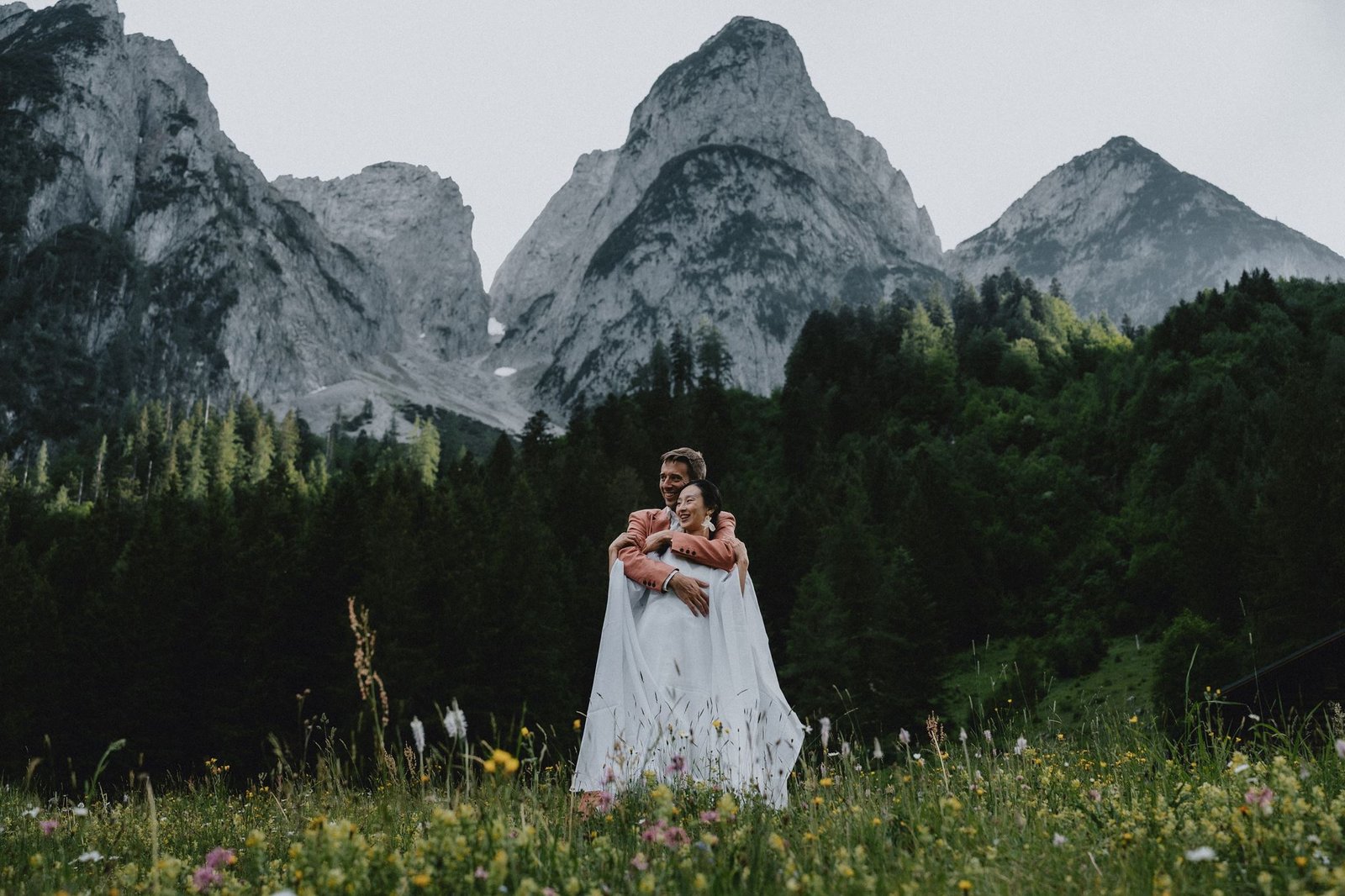 Elias und Wendy umarmen sich auf einer Wiese unter schroffen Berggipfeln.