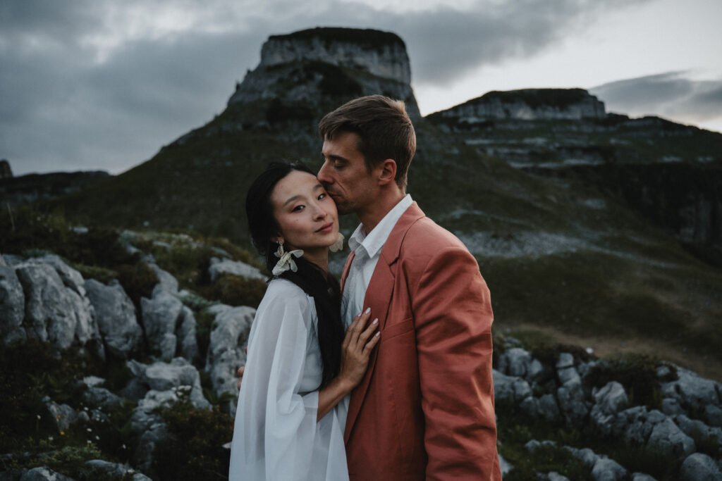 Elias and Wendy embracing among rocks beneath a mountain peak.