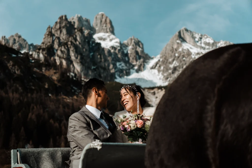 Couple smiling at each other beside a horse with jagged mountains behind them.