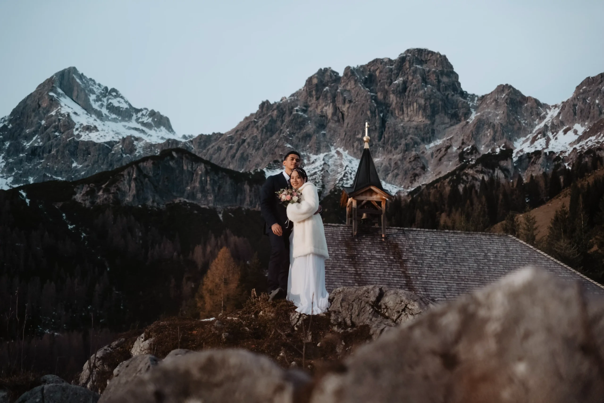Paar über einem Bergsee zwischen verschneiten Gipfeln.
