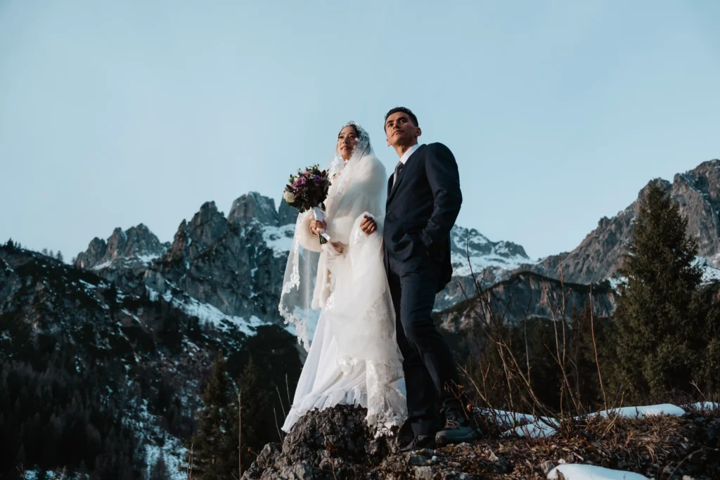 Bride and groom standing on a rocky ridge beneath a clear winter sky.