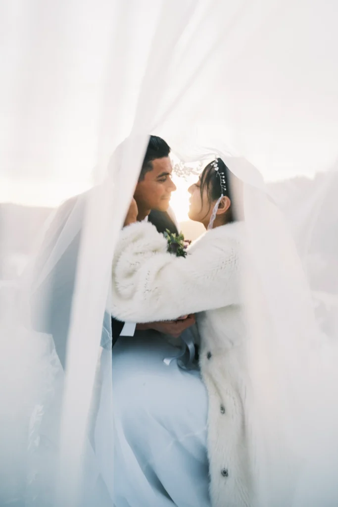 Couple embracing beneath a translucent bridal veil in the snow.
