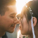 Close portrait of a couple touching foreheads with sunlight between their faces.