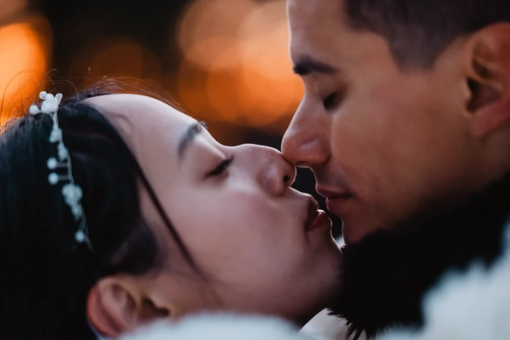 Close portrait of a couple kissing against warm evening lights.