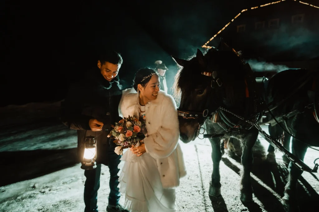 Couple holding a lantern beside a horse at night in the snow.