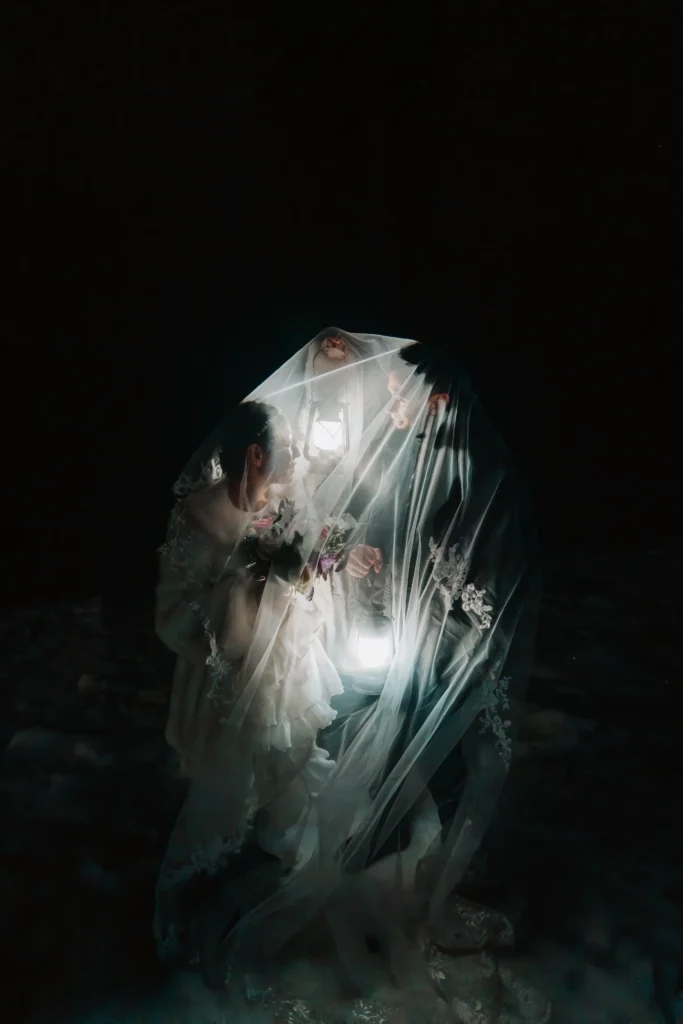Vertical night portrait of a couple beneath an illuminated veil.