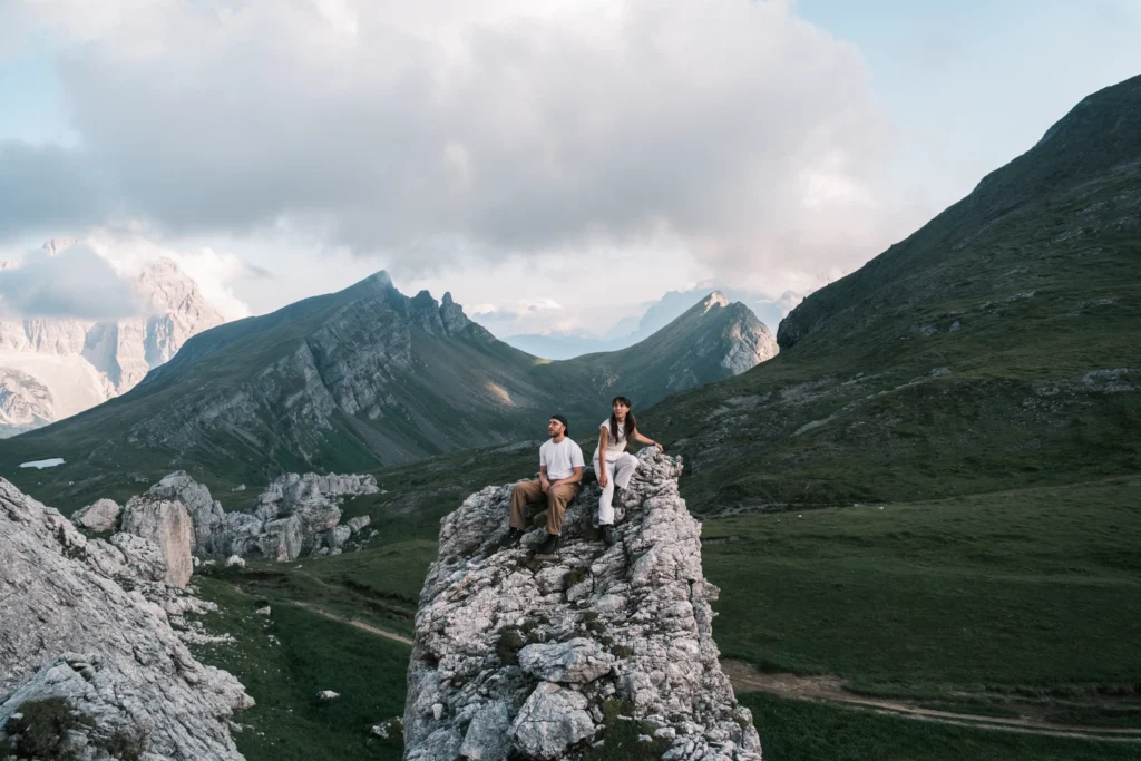 Couple sitting together on a rocky outcrop above a green mountain valley.