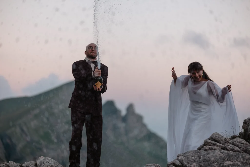 Couple celebrating with champagne on a mountain ridge.