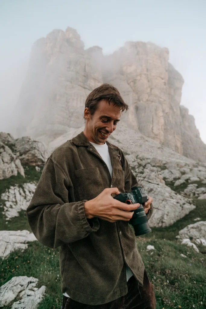 Elias holding his camera beneath a rocky mountain peak.