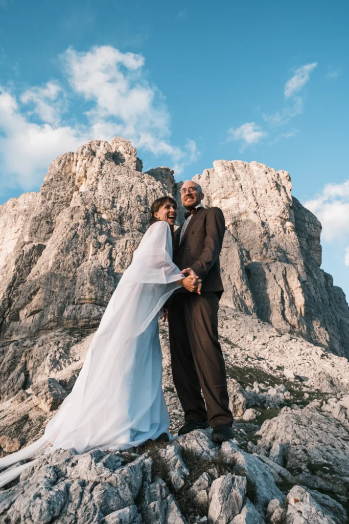 Couple in wedding attire embracing beneath rugged mountain peaks.