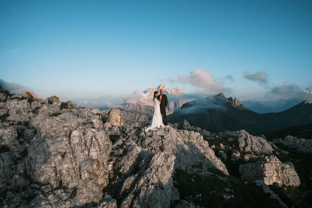 Couple standing on a high rock ledge above the mountain landscape.