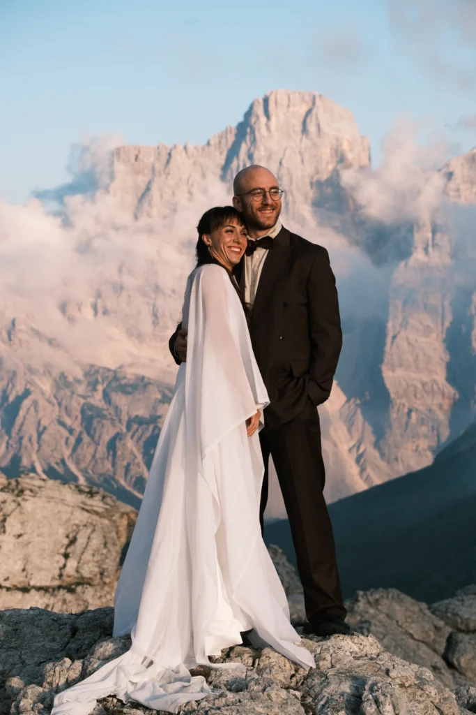 Couple in wedding attire standing together beneath towering limestone peaks.