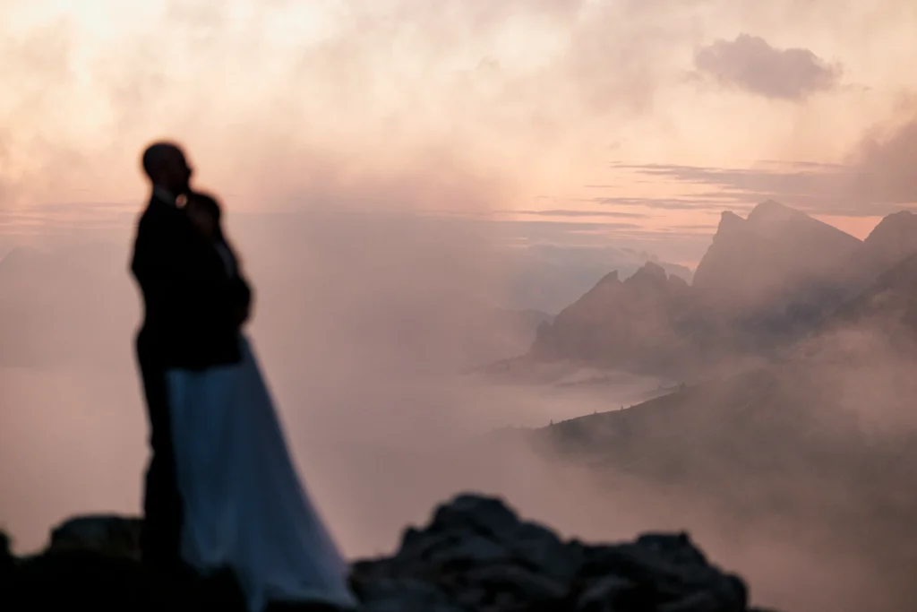 Soft-focus portrait of a bride looking across misty mountain peaks in warm evening light.