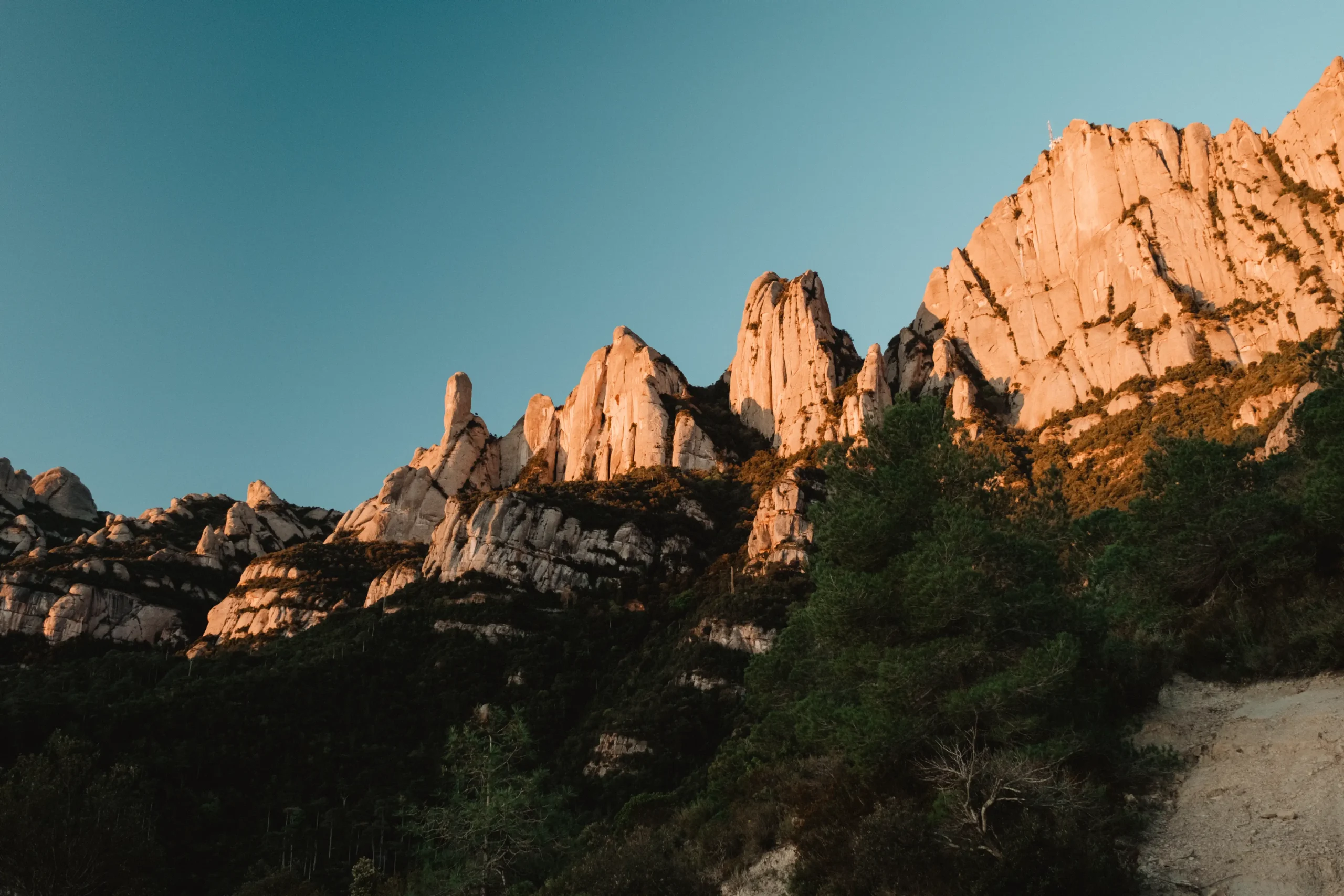 Sonnenaufgang über schroffen Felstürmen neben einem Bergweg.