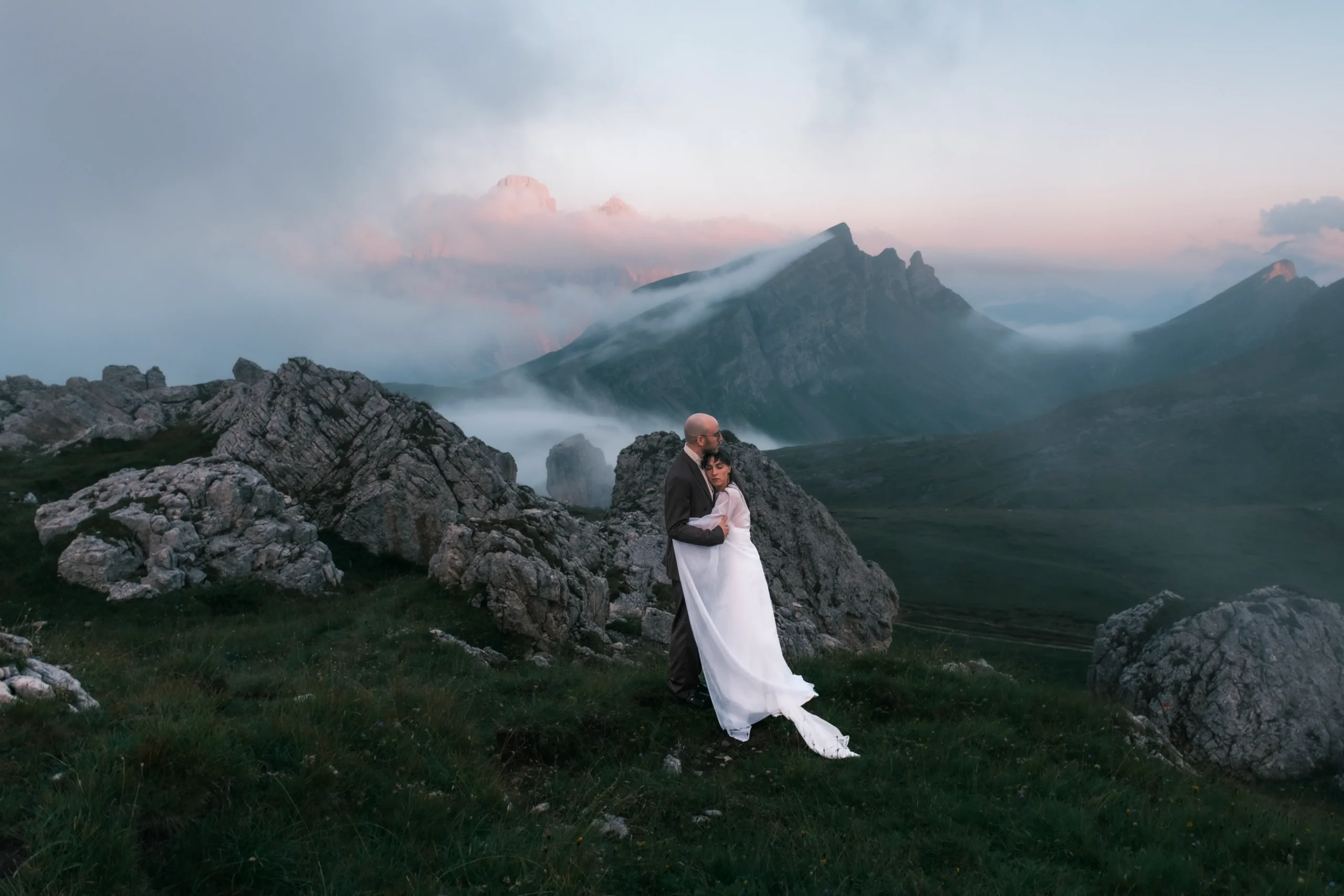 Couple embracing among rocks above a misty mountain valley.